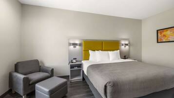 Una habitación de hotel con una cama grande, un sofá gris, una mesita y una mesita de noche con una lámpara.