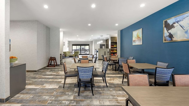 Un área de comedor moderna con varias mesas y sillas, una encimera de cocina y una pared azul decorada con obras de arte.