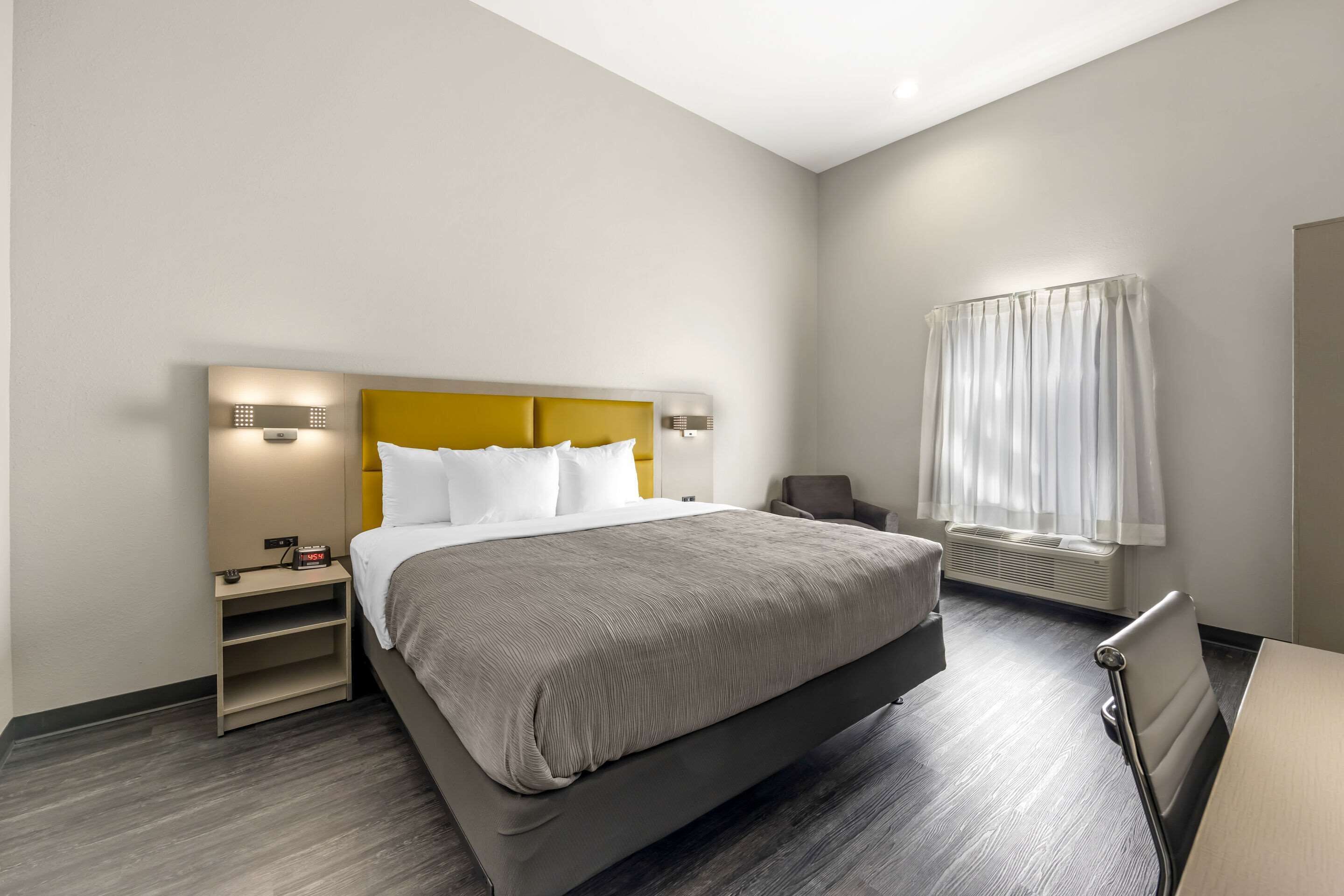 A modern hotel room with a large bed, a bedside table, a chair, and a window with curtains.