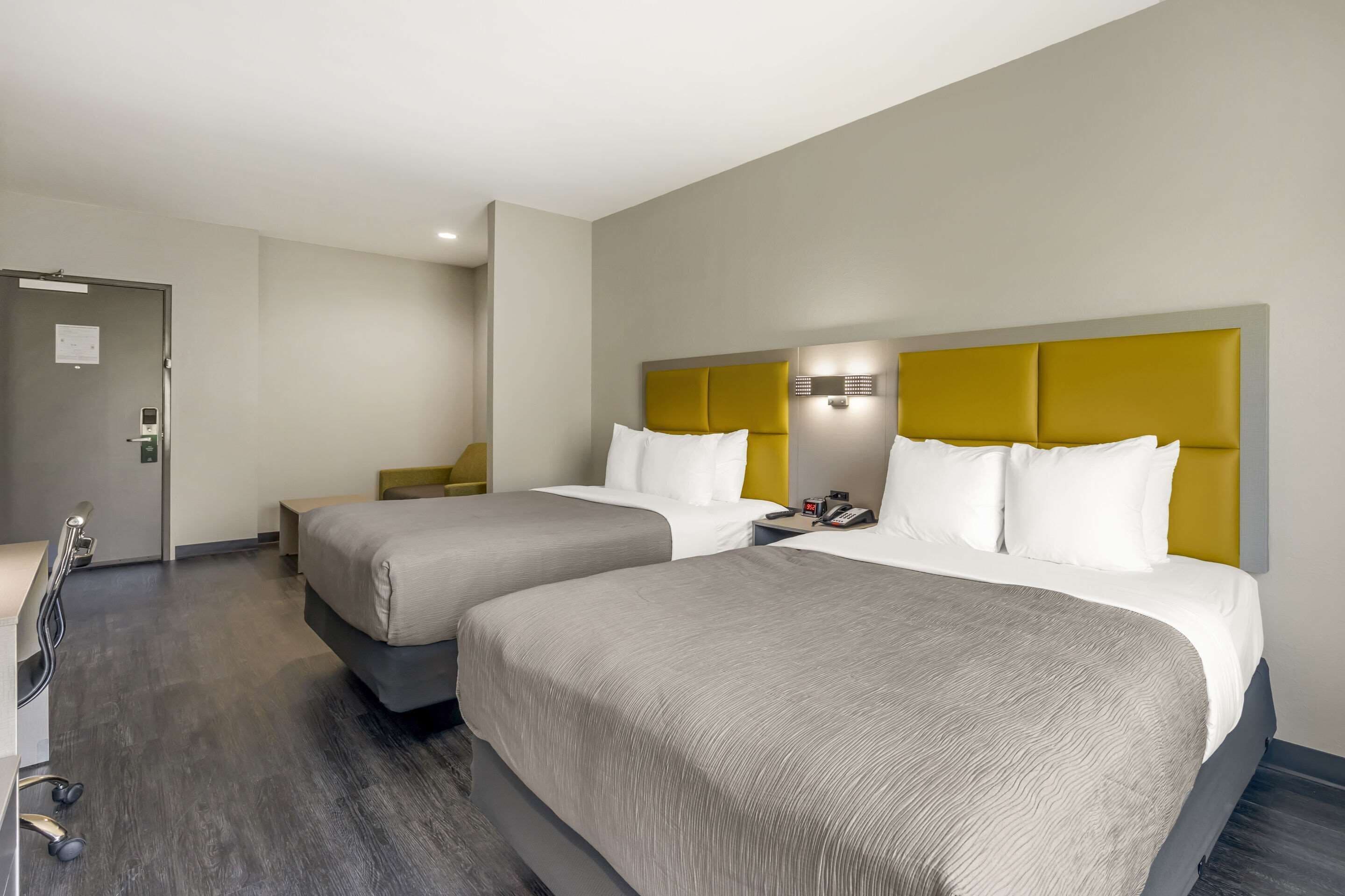 Et hotelværelse med to senge, et skrivebord og et bruseområde.