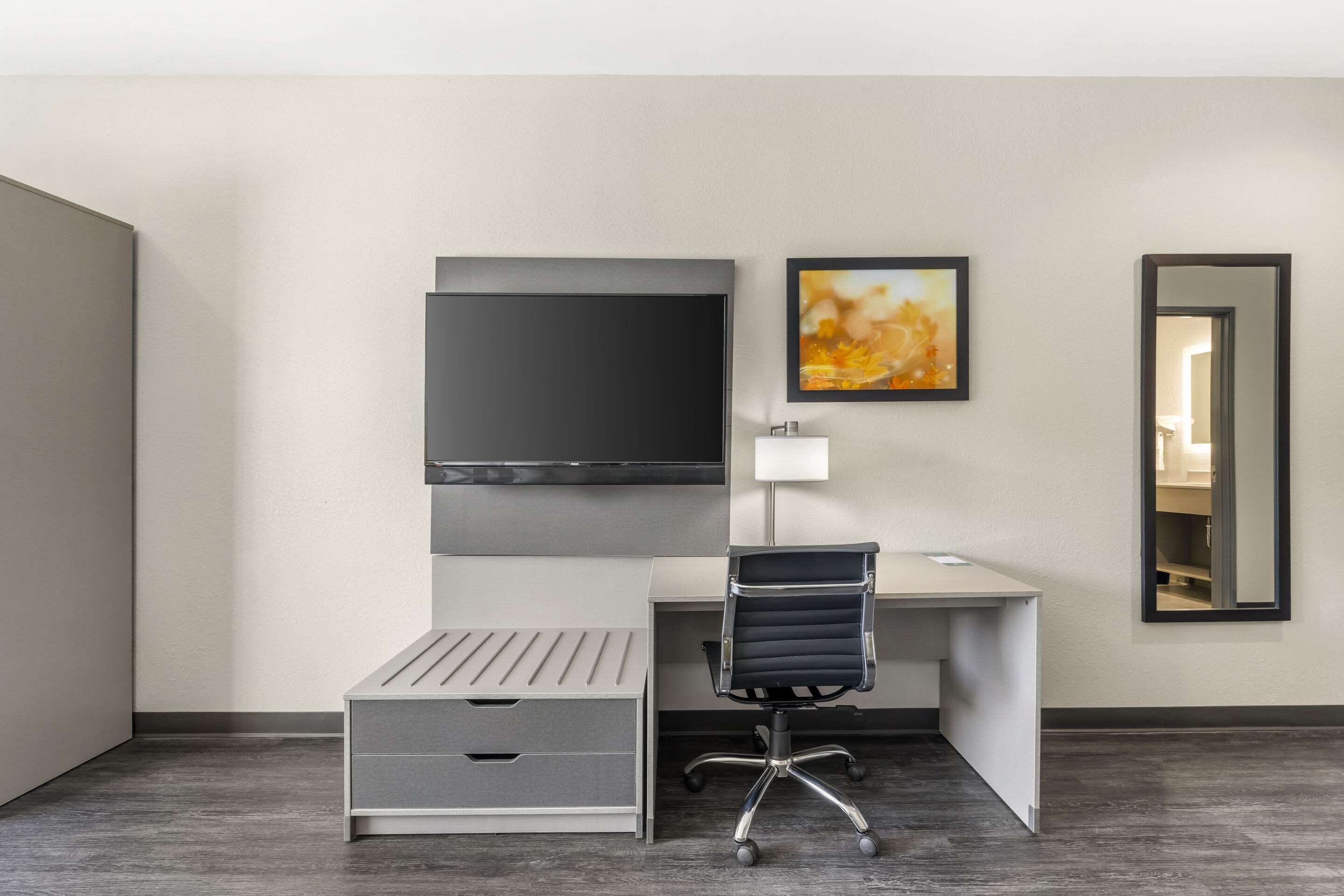 A modern hotel room with a desk, chair, and a large flat-screen TV mounted on the wall.