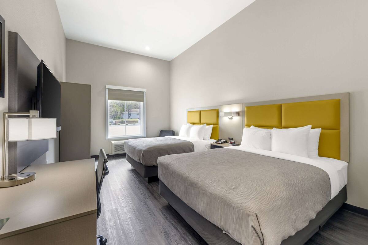 Habitación de hotel con dos camas, un escritorio con lámpara, televisor y ventana con vistas al exterior.
