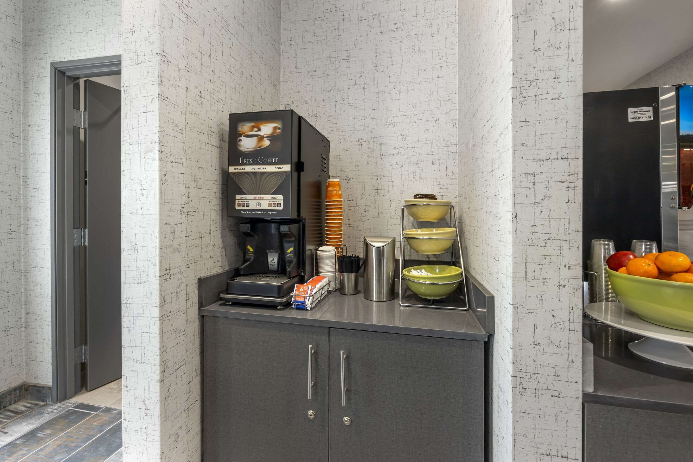 A coffee station with a coffee machine, stacked cups, and bowls of fruit.