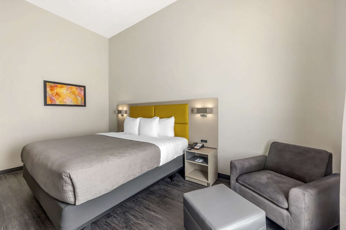 Una habitación de hotel con cama, mesita de noche, una silla y una pequeña mesa.