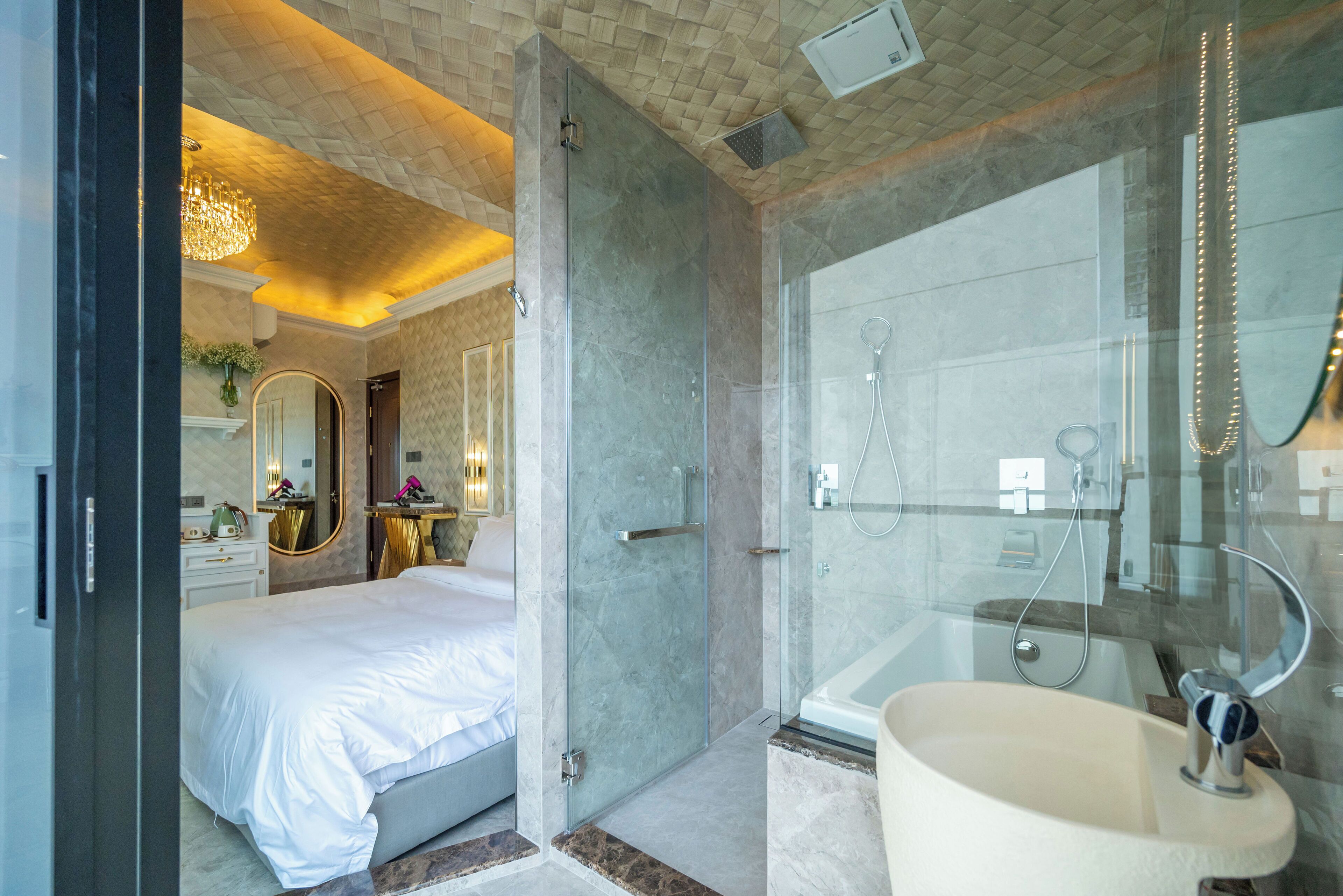A modern hotel bathroom with a glass-enclosed shower, a large bathtub, and a separate vanity area.