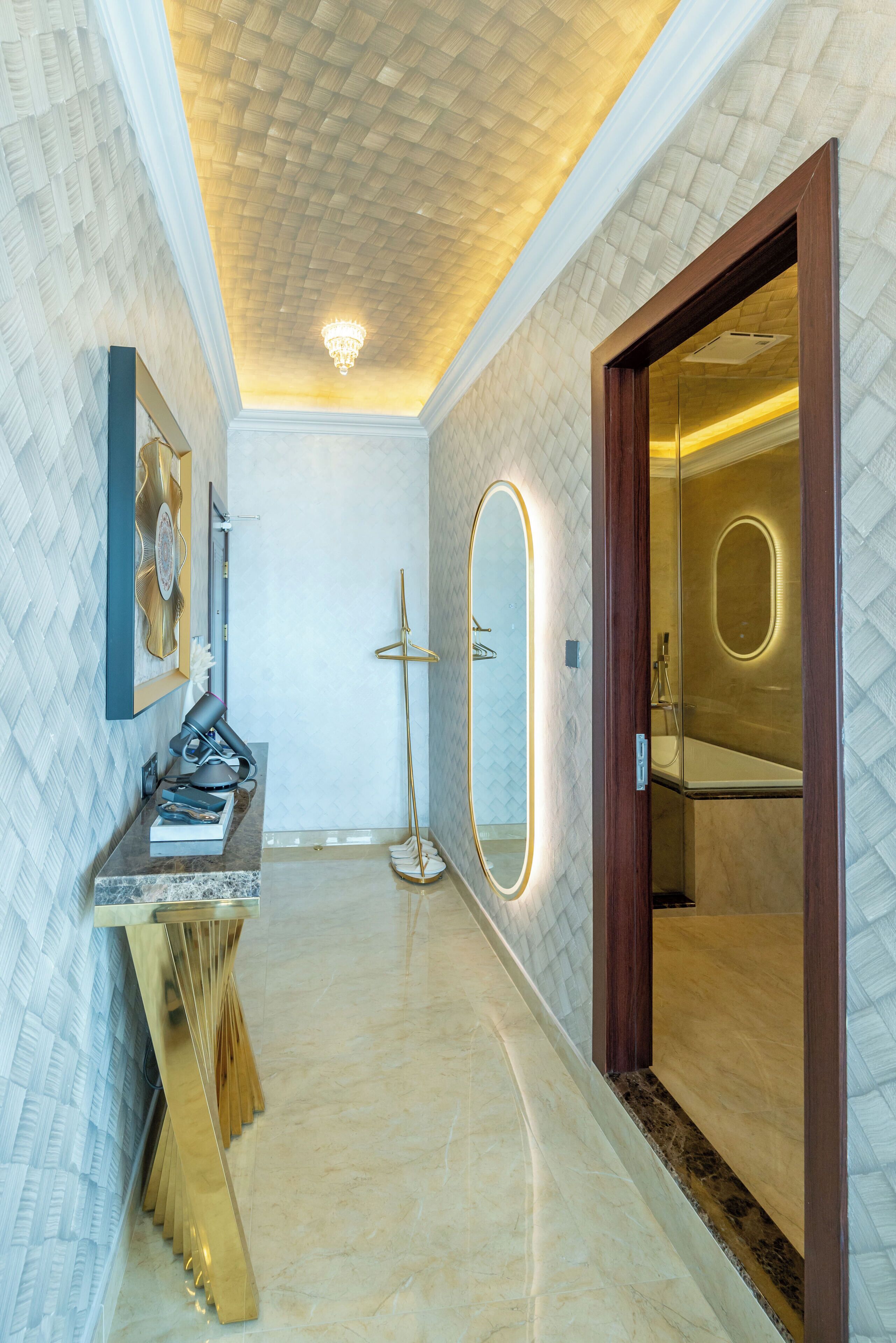 A hallway with a marble floor, a wooden floor lamp, a mirror, and a door leading to a bathroom.