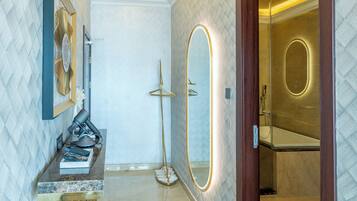 A hallway with a marble floor, a wooden floor lamp, a mirror, and a door leading to a bathroom.