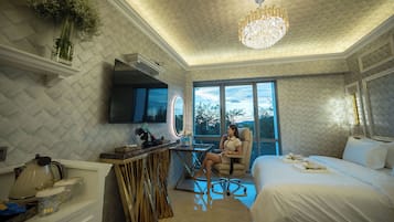 A hotel room with a large bed, a sitting area with a chair, a desk with a mirror, and a view of the outdoors.