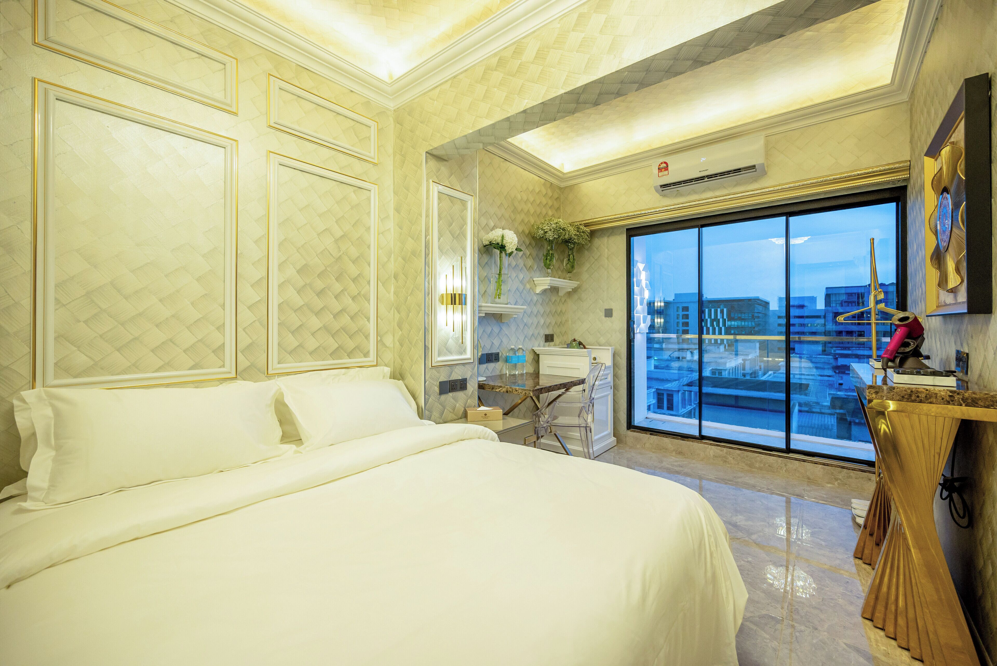 A hotel room with a large bed, a desk, and a view of the city through a large window.