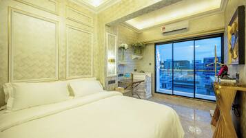 A hotel room with a large bed, a desk, and a view of the city through a large window.