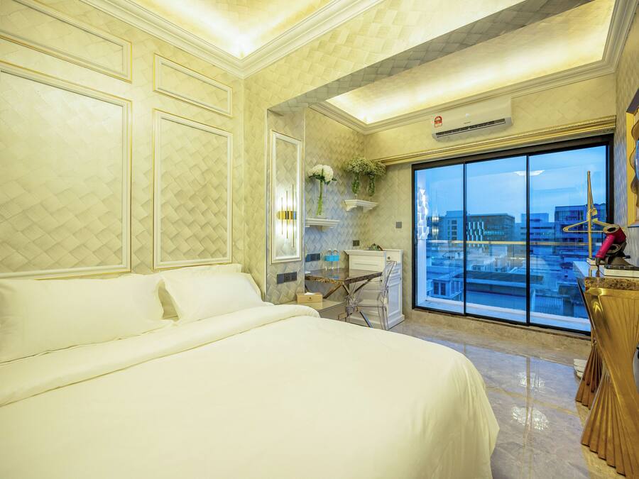 A hotel room with a large bed, a desk, and a view of the city through a large window.