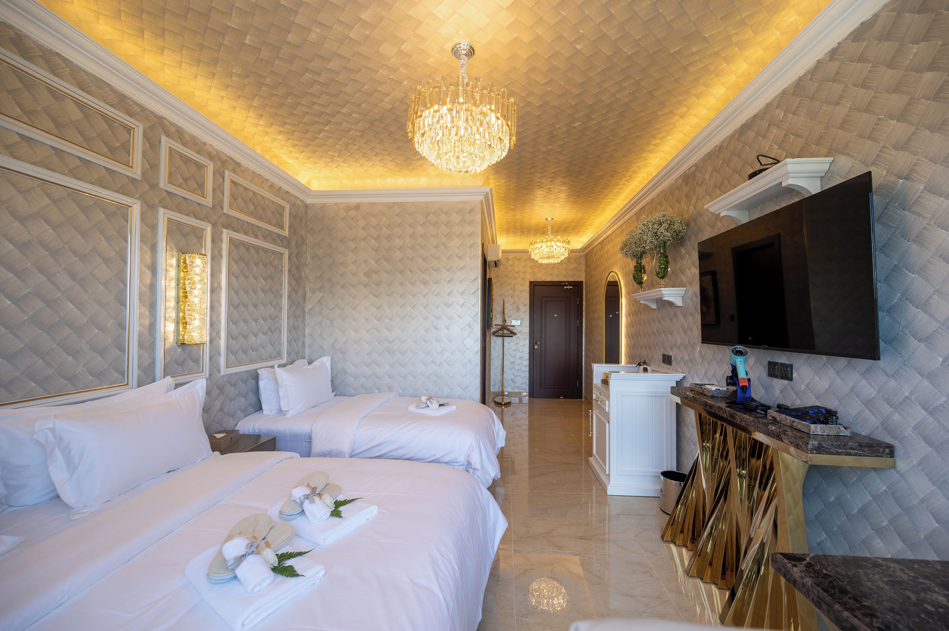 A hotel room with two beds, a TV, a minibar, and a chandelier.