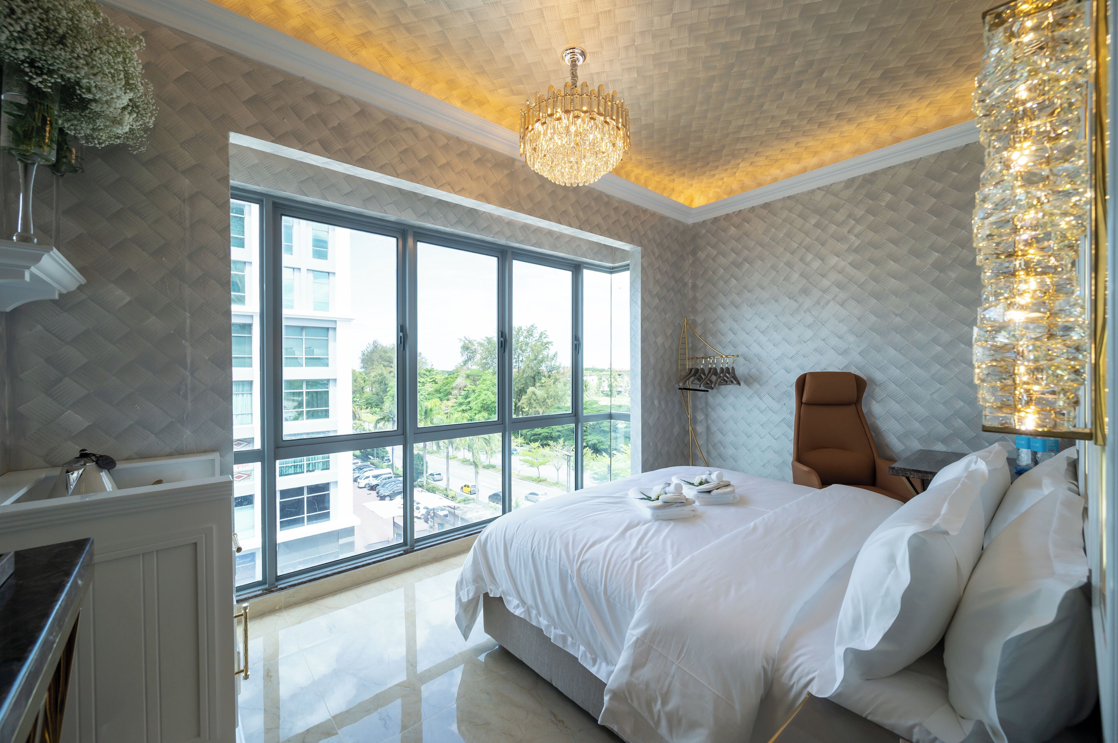 Una habitación de hotel moderna con un ventanal grande, una araña y una cama con sábanas blancas.