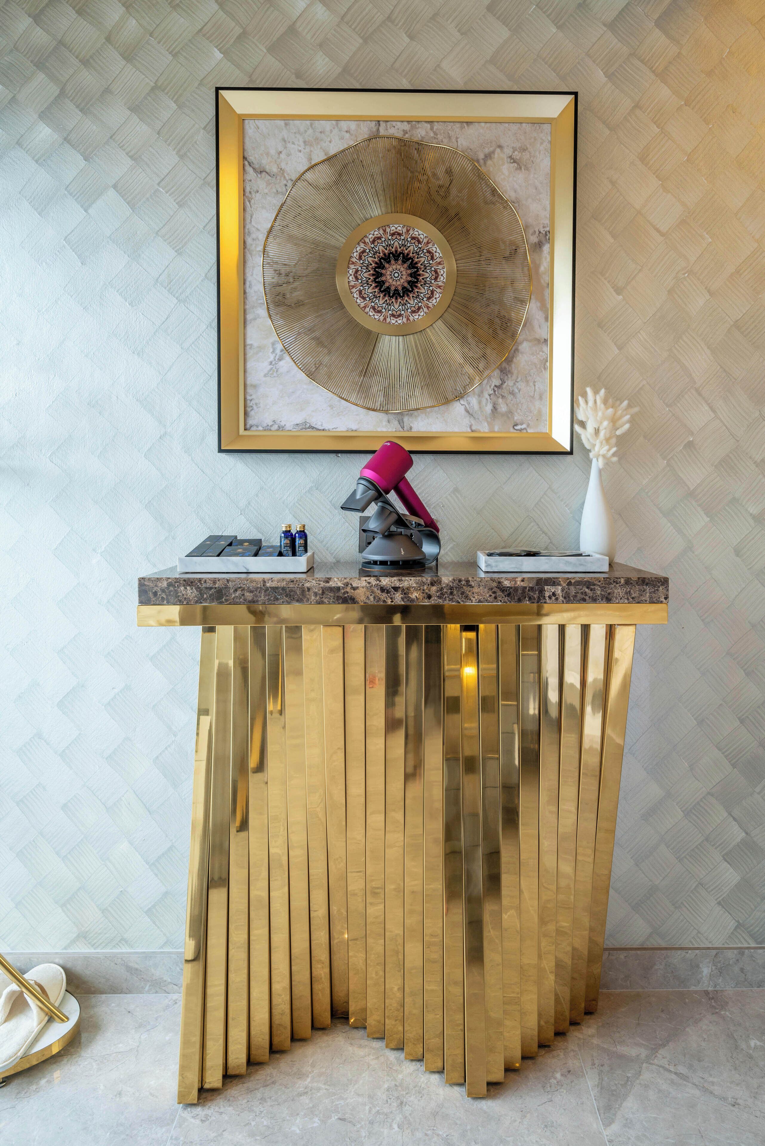 A reception desk with a framed artwork above, a vase with white flowers, and a pair of white slippers on the floor.