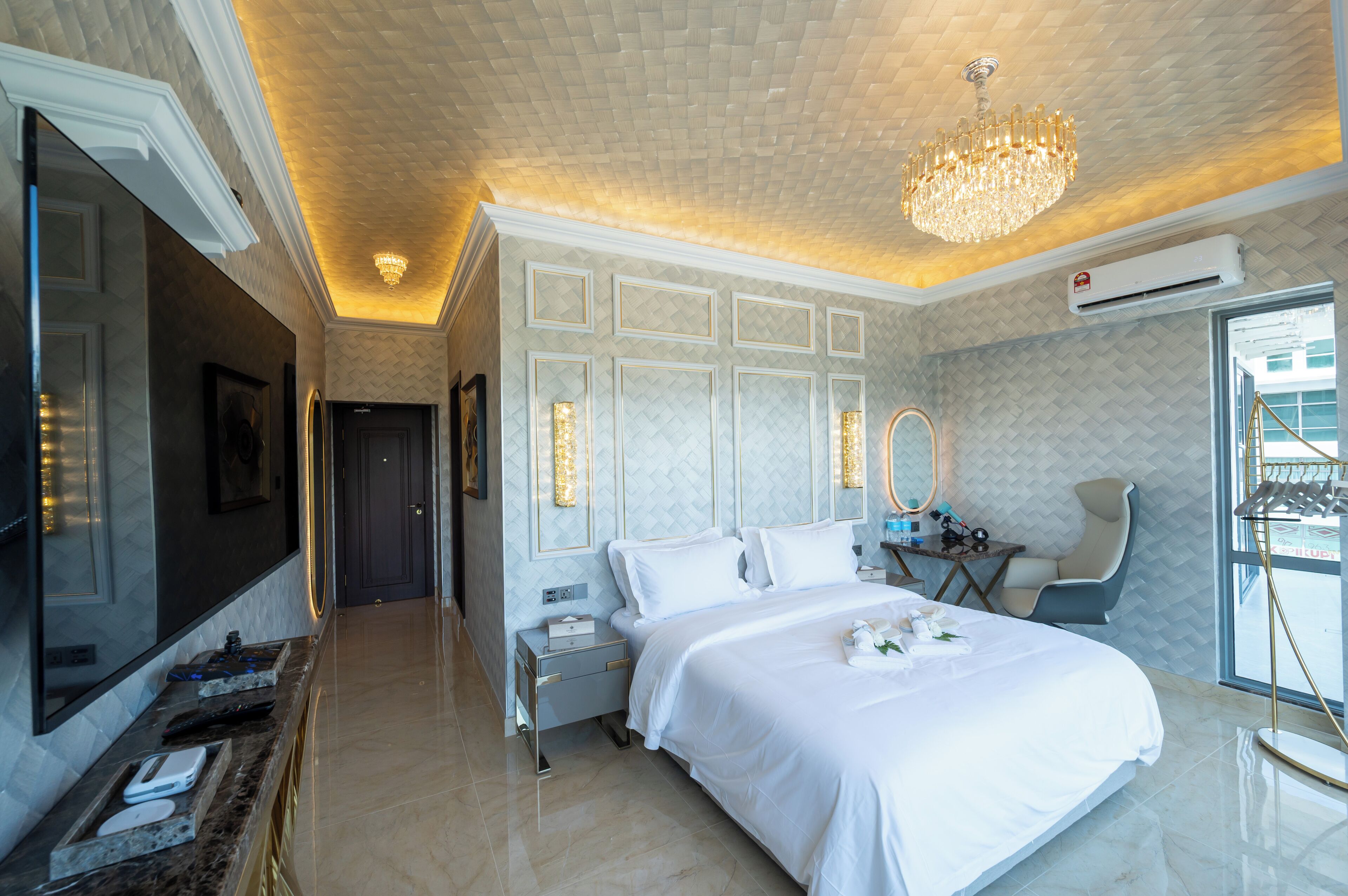 A modern hotel room with a large bed, a sitting area with a chair, a vanity with a mirror, and a television.