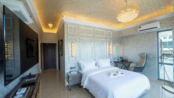 A modern hotel room with a large bed, a sitting area with a chair, a vanity with a mirror, and a television.