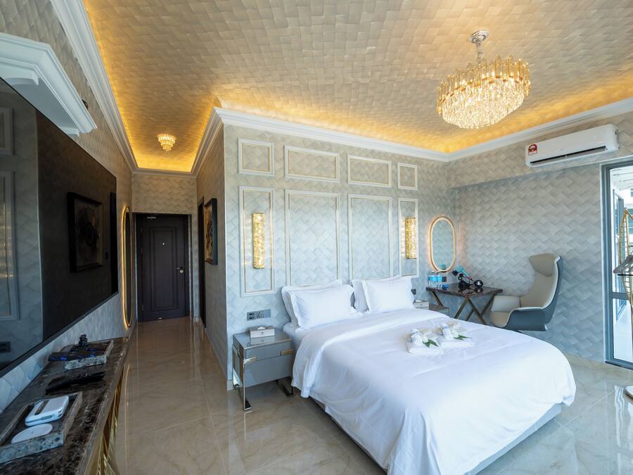A modern hotel room with a large bed, a sitting area with a chair, a vanity with a mirror, and a television.