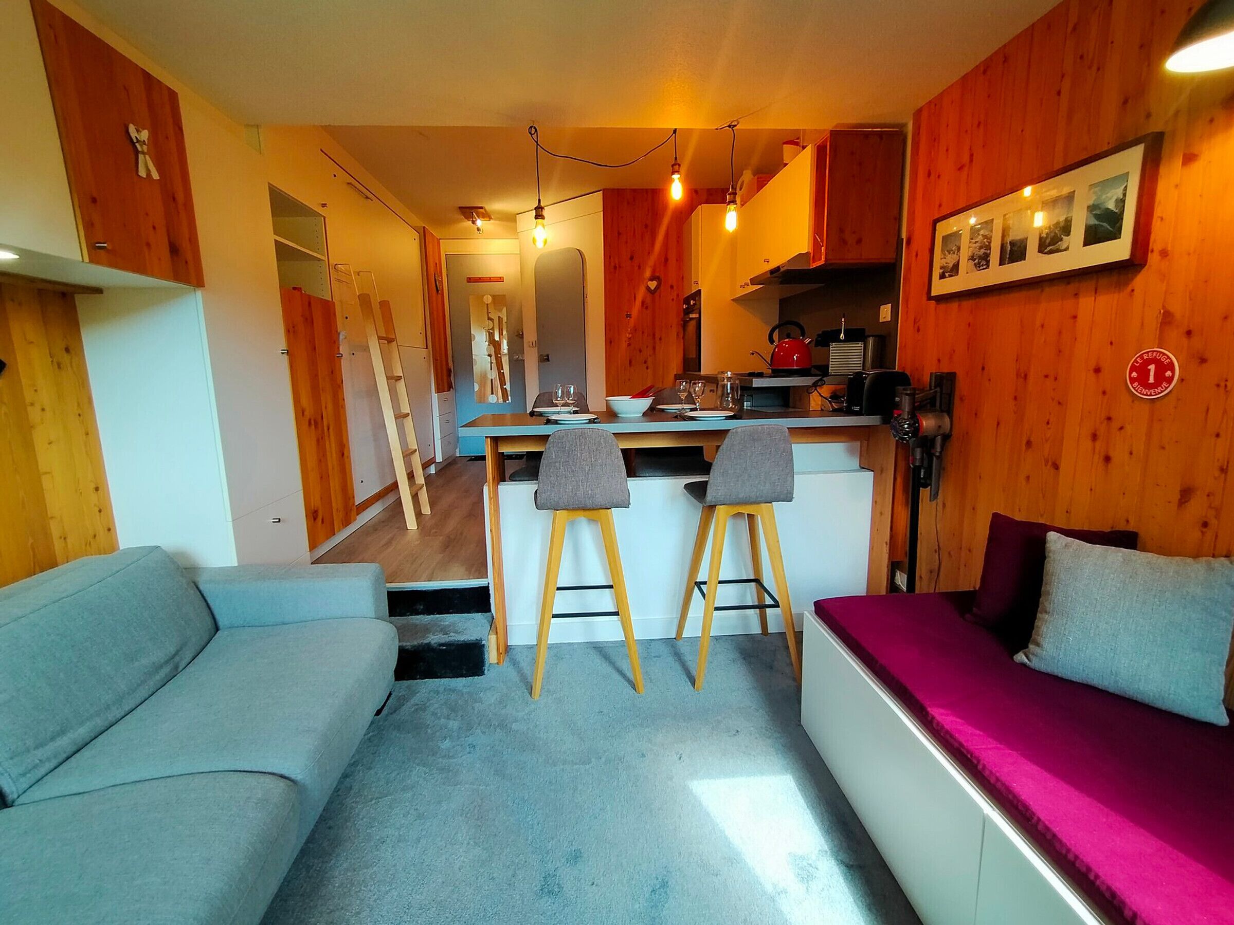 A compact living space with a kitchenette, a sofa, a dining area, and a staircase leading to an upper level.