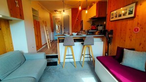 A compact living space with a kitchenette, a sofa, a dining area, and a staircase leading to an upper level.