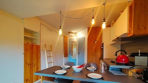 A compact kitchen with wooden cabinets, a dining table set for two, and a red kettle on the counter.