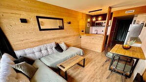 Un espacio habitable compacto con sofá, una pequeña mesa, kitchenette y zona de comedor.