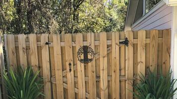 Une porte en bois ornée d’un motif métallique décoratif, flanquée de plantes en pot, mène à une maison dont le toit est en pente.