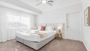 Moderni hotellihuone, jossa on suuri sänky, yöpöytä lampun kanssa ja ovi.