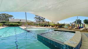 A swimming pool with a sunshade, lounge chairs, and a children's play area.