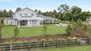 A two-story house with a covered patio, a lawn, and a wooden fence.