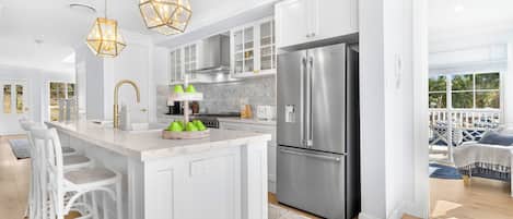 A modern kitchen with white cabinetry, a stainless steel refrigerator, and a central island with bar stools.