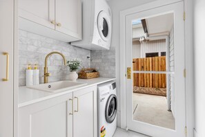 A compact kitchen with a washing machine, a sink with gold faucets, and a potted plant.