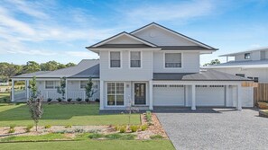 A two-story house with a garage, a well-maintained lawn, and a gravel driveway. - MONTAUK HOUSE - THE VINTAGE HOLIDAY HOUSES (POKOLBIN)