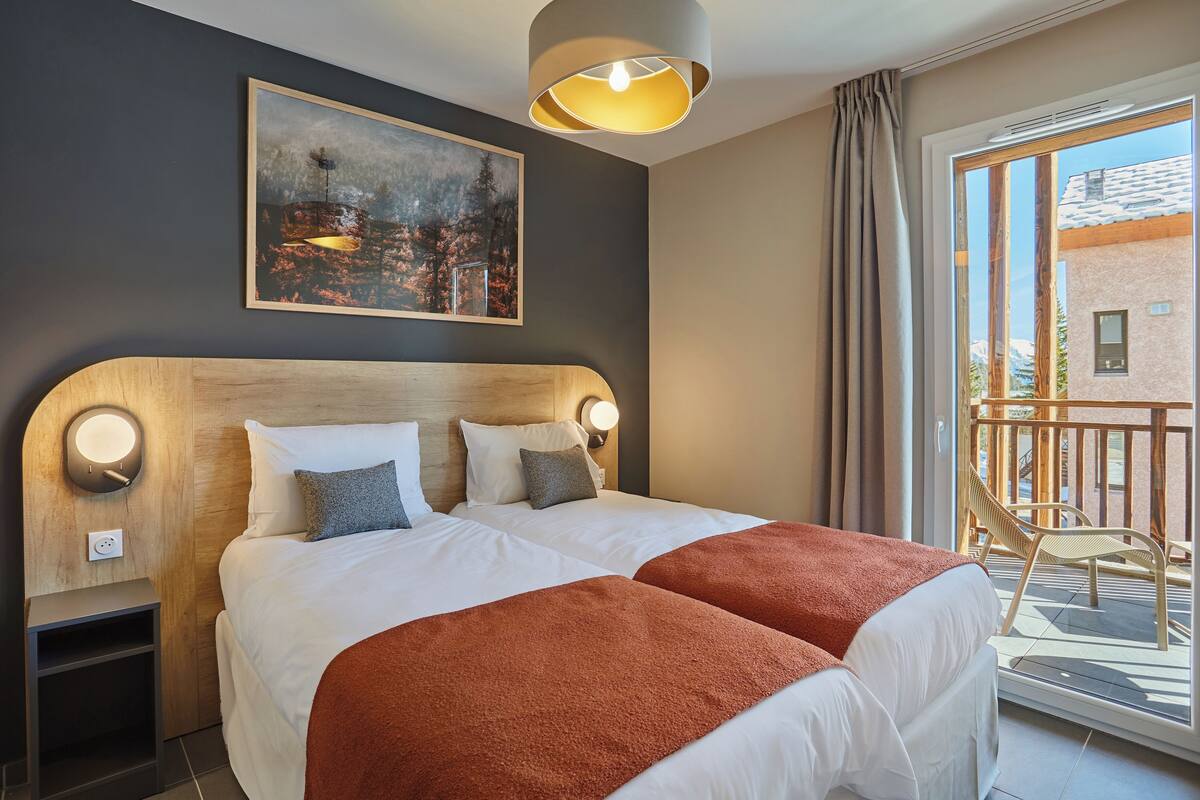 A double bed with a wooden headboard, two bedside lamps, and a painting above.