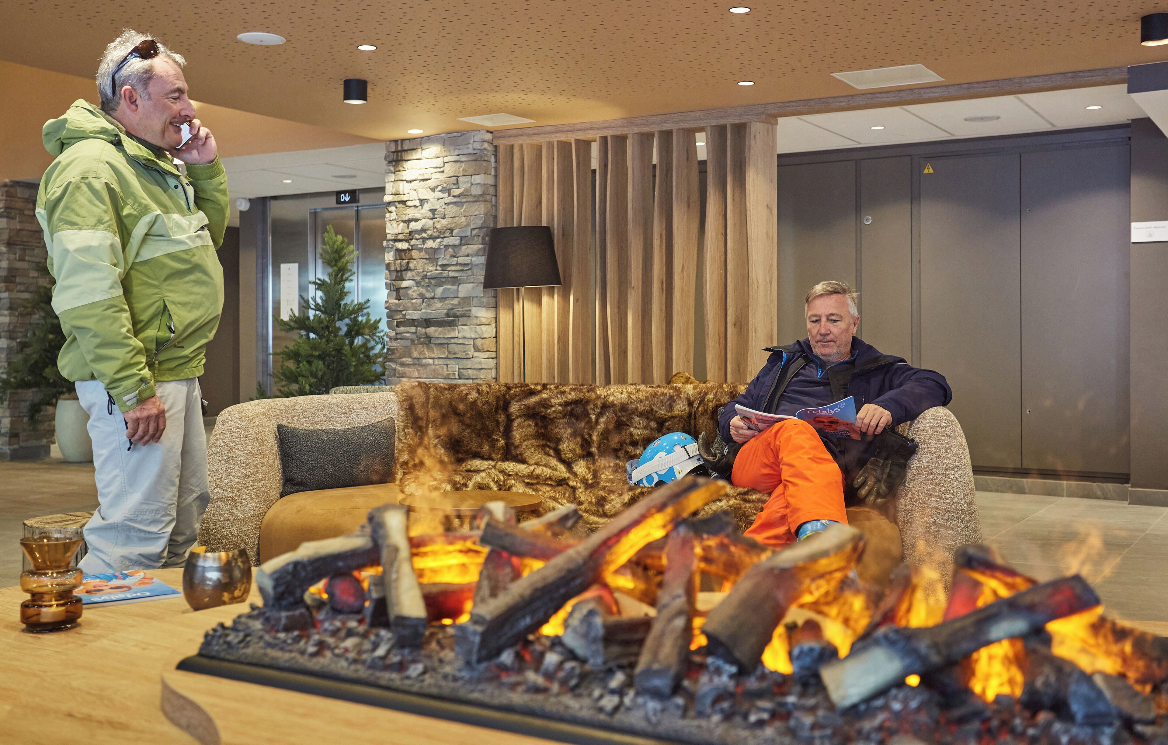 A lobby with a stone wall, a wooden panel wall, and a fireplace with logs.