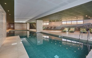 A modern indoor swimming pool with clear water, lounge chairs, and a mural of mountains on the wall. - Résidence  Odalys Le Mont dAuron (Saint-Etienne-de-Tinee)