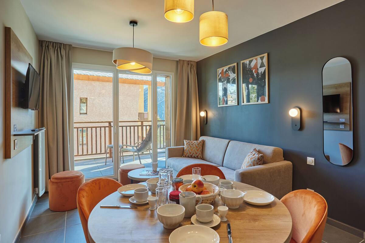 A modern living room with a dining area, a sofa, a TV, and a balcony with a view.