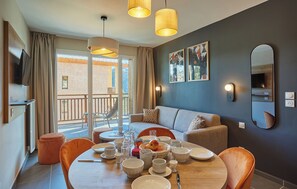 A modern living room with a dining area, a sofa, a TV, and a balcony with a view. - Résidence  Odalys Le Mont dAuron (Saint-Etienne-de-Tinee)