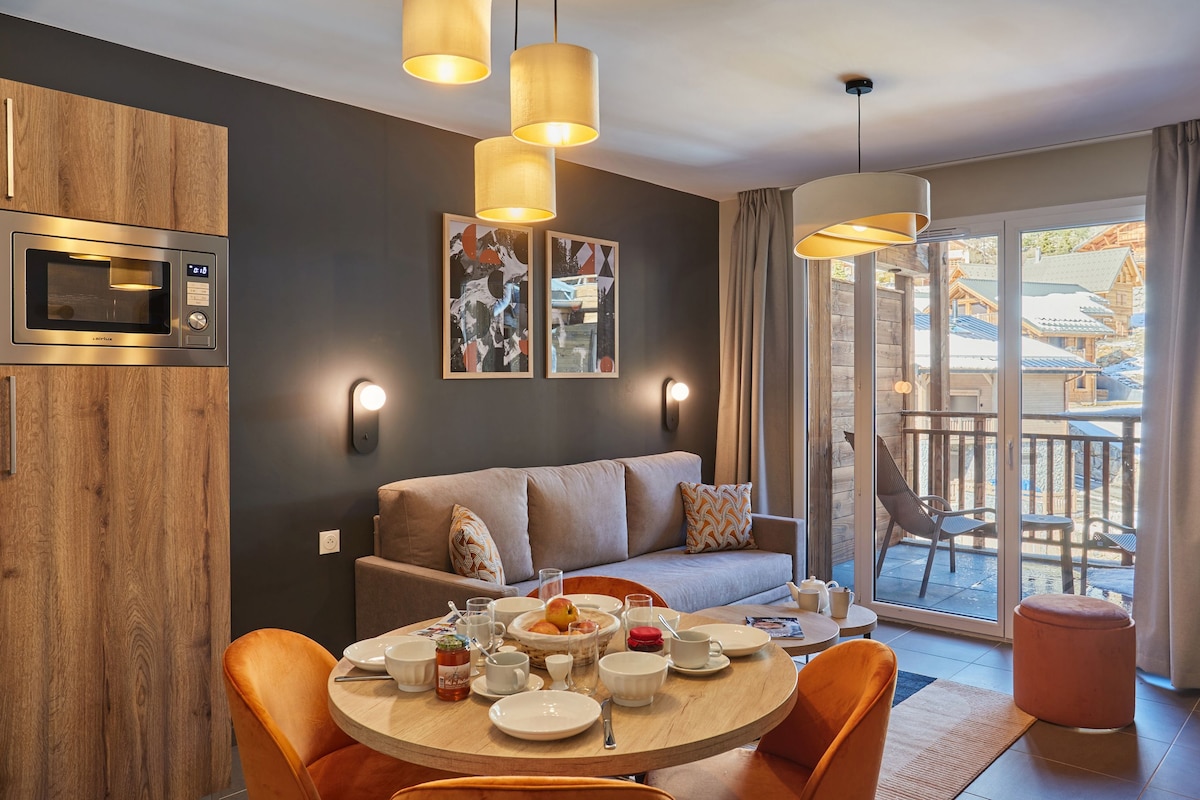 A modern kitchen with a built-in microwave, wooden cabinets, and a dining area with orange chairs and a round table set for breakfast.