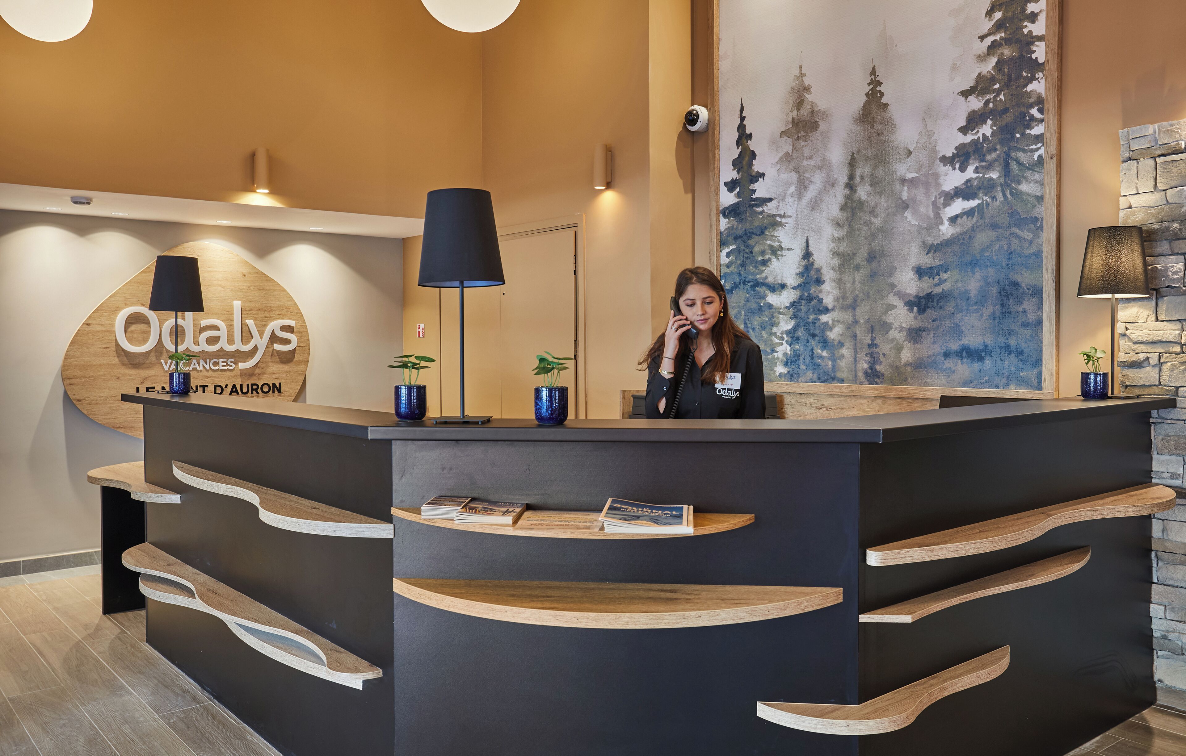 A reception desk with a wooden design, a large sign reading "Odalys Vacances," and a painting of trees on the wall.