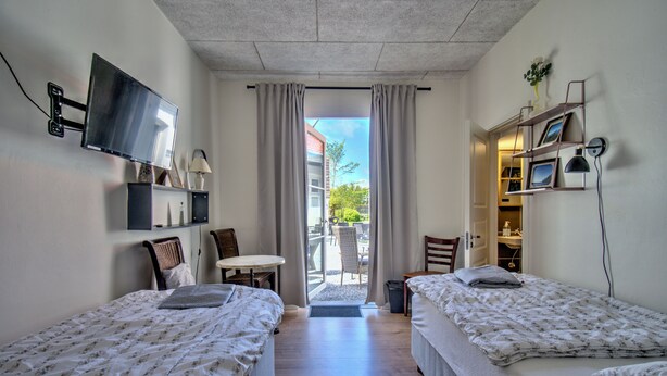 A room with two beds, a TV, a desk, and a view of the outside. - Marielyst Sleep and Go (Vaeggerlose)