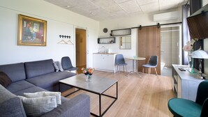 A modern living room with a grey sofa, a coffee table, and a dining area with a small table and chairs. - Marielyst Sleep and Go (Vaeggerlose)