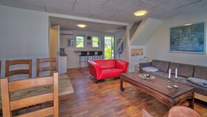 A spacious living area with a wooden dining table, a red leather sofa, and a brown sofa. There is a kitchen in the background with a bar counter and chairs. - Marielyst Sleep and Go (Vaeggerlose)