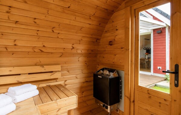 Une salle de sauna en bois, avec un banc et des serviettes, un appareil de chauffage pour sauna, et une vue sur un bâtiment rouge à l’extérieur.