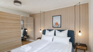 Una cama bien hecha con sábanas blancas, un cabecero azul y un cuadro en la pared.