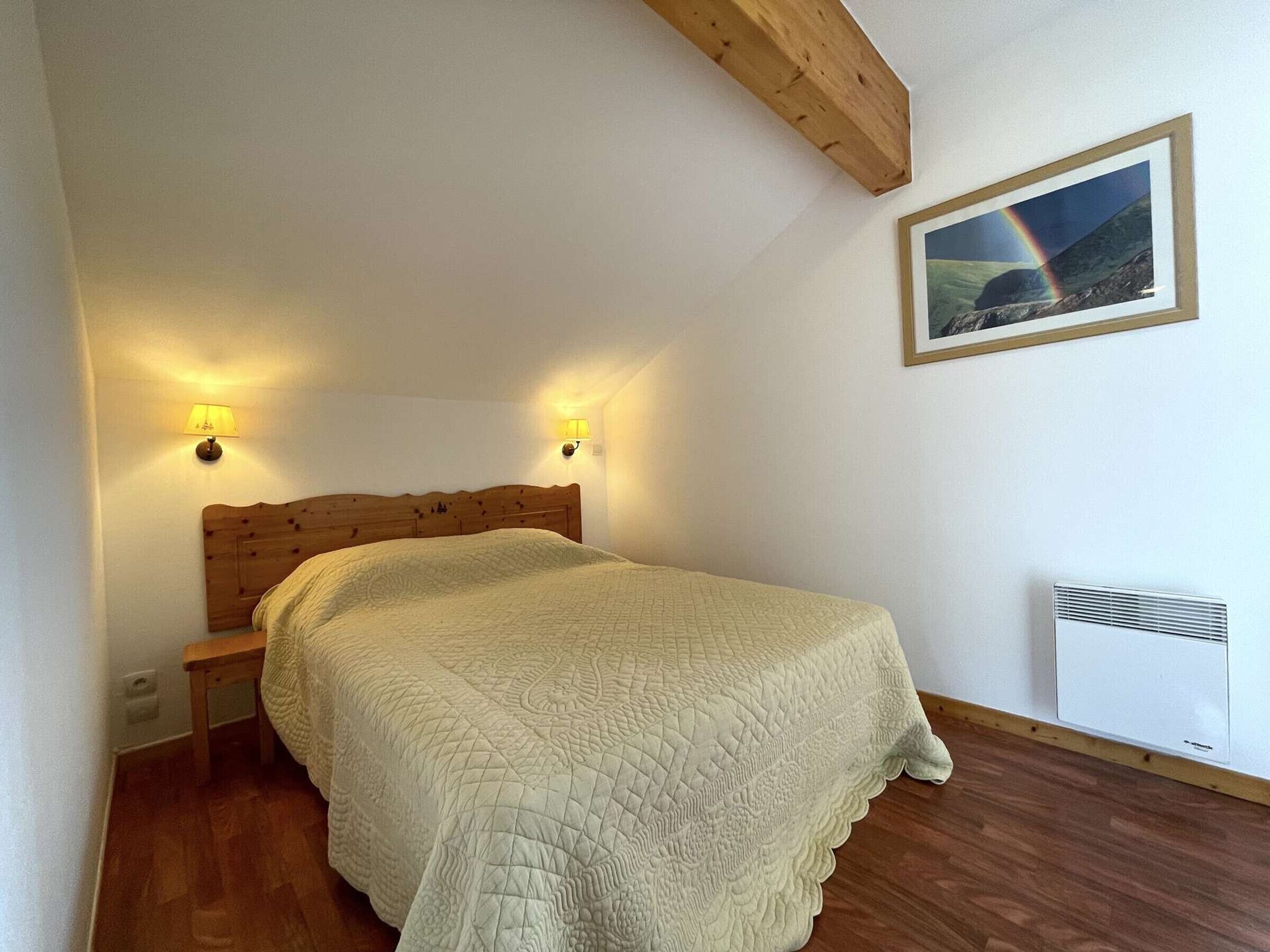 A bedroom with a wooden headboard, two bedside lamps, a quilted bedspread, a framed picture on the wall, and a radiator.