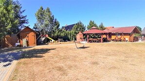 A rustic outdoor area with a wooden play structure, a swing set, and a covered seating area.