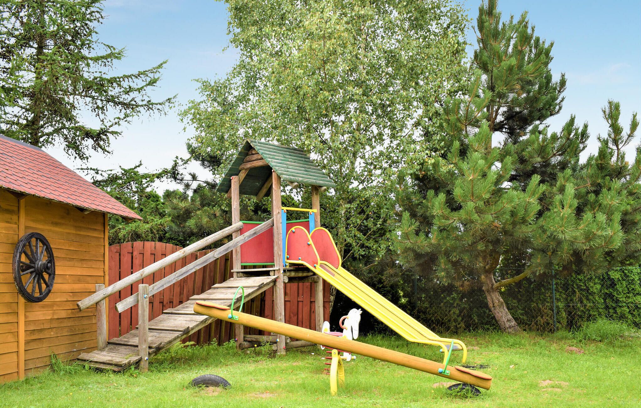 Une cabane en bois avec un toboggan, une balançoire et une balançoire faite d’un pneu, le tout installé dans un espace verdoyant avec des arbres.