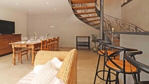 Un comedor con una mesa de madera preparada para cuatro personas, un sofá y una escalera con barandilla metálica.