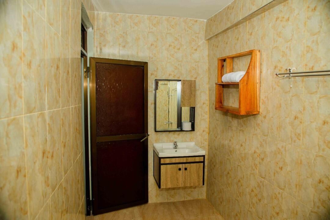 A bathroom with a marble wall, a wooden door, a sink with a mirror, and a towel rack.