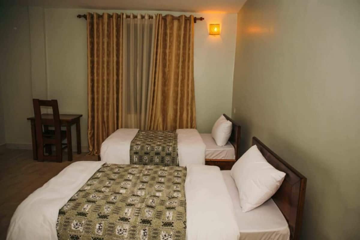 Una habitación de hotel con dos camas, una silla y una lámpara fijada a la pared.